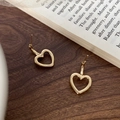 Detail view of hollow heart-shaped gold-plated earrings on a rustic wooden background - Gold