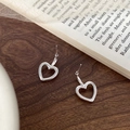 Detail showing high-polished hollow heart stud earrings on a vintage wooden surface - Silver