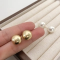 Detail van minimalistische ronde gouden oorknopjes en witte parelbollen op beige fluweel - Mat Goud (Echt Verguld)