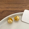 Primer plano de pendientes geométricos de bola en oro mate sobre plato de cerámica - Pendiente de Bola / Oro Mate Cepillado