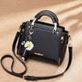 Elegante bolso de piel negra con asa dorada, correa ajustable y colgante de margarita - Negro