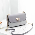 Grey patchwork crossbody bag with pearl cat pendant and gold chain strap on table - Gray