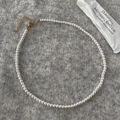 Detailopname van een ronde witte parelketting met gouden sluiting op grijs breisel - 4mm Ronde Schelpparel Ketting