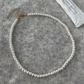 Detail van ronde parelketting met gouden sluiting op een grijze gebreide achtergrond - 5mm Ronde Schelpparel Ketting
