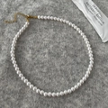 Detailopname van een ronde witte parelketting op grijs vilt met een gouden sluiting - 6mm Ronde Schelpparel Ketting