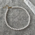 Detailopname van witte parelketting met gouden sluiting op grijze gebreide achtergrond - 8mm Ronde Schelpparel Ketting
