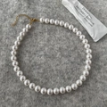 Detail view of round white pearl necklace with golden lobster clasp on textured fabric - 10mm Round Shell Pearl Necklace