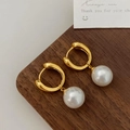 Detail of 18K gold pearl drop earrings on a wooden stand with high-polished finish - Gold