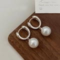 Detailed close-up of geometric silver hoop earrings with white pearls on a wood surface - Silver