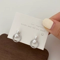 Detail of elegant double pearl earrings with zircon-paved ring held in hand - Silver