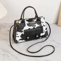 Elegante borsa con stampa mucca, tracolla nera e logo dorato su marmo - Stampa Mucca