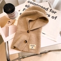Dettaglio passamontagna in maglia con bottoni in corno ed etichetta su tessuto beige - Albicocca