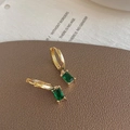 Détail de créoles dorées avec pierres de zircone vert émeraude sur un tapis texturé - Boucles d'Oreilles Pendantes en Zircone Carrée Vert Émeraude Doré
