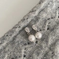 Detail der unregelmäßigen silbernen Ohrringe mit runder Perle auf grauem Strick - Silber
