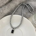 Primo piano di una collana di perle con ciondolo in pietra nera su un piatto di ceramica - Collana Perla Grigia Zircone Nero