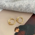 Detaillierte Draufsicht auf vergoldete Knoten-Ohrringe auf texturiertem Stoffhintergrund - Geknotete Glatte Ohrringe (Vergoldet) / Gold
