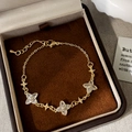 Dettaglio di un braccialetto a quadrifoglio dorato con zirconi su velluto marrone scuro - Bracciale con zirconi e fiori di quadrifoglio dorati