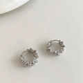 Detalle de pendientes de aro plateados con textura ondulada sobre fondo minimalista - Plateado