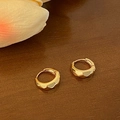 Nahaufnahme facettierter goldener Creolen mit geometrischen Kanten auf Holzgrund - Gold