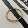 Dettaglio del bracciale dorato con strati metallici ondulati e perle lucide alle estremità - Bracciale rigido aperto dorato texture argento frantumato