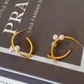 Detalle de pendientes en C dorados con diseño cruzado y tres perlas blancas - Perla Cruzada Dorada (Chapado en Oro Real)