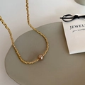 Detalle de collar de cadena dorada trenzada con colgante de perla marrón sobre soporte - Collar Dorado (Con Perla Champán)