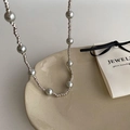Detailed shot of silver-tone twisted metal chain necklace with grey pearls on ceramic plate - Silver