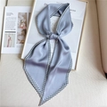Dettaglio di un foulard in raso blu-grigio con bordo pied de poule su sfondo di libri - Grigio Morandi
