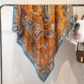 Orange paisley silk scarf with blue borders hanging on a metal rack display - Bright Orange Paisley (FE138-1)