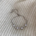 Dettaglio di un bracciale argento regolabile con zirconi scintillanti su sfondo in maglia - Argento