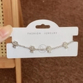 Gros plan d'un bracelet croix en argent serti de zircons brillants sur carte de vente - Style Croix (Bracelet Fleur à Quatre Feuilles Argenté) / Argenté