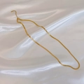 Close-up of gold snake bone chain necklace lying on white satin fabric background - Gold Short Flat Herringbone Necklace