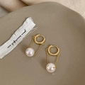 Detail of gold-plated pearl drop earrings with slender chains on a ceramic tray - White