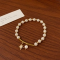 Detail of pearl bracelet with gold spiral bar and sparkling starburst pendant on wood - Star Charm Style