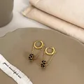 Close-up of gold dangle earrings with black zircon cylinders on a ceramic tray - Gold Black Hoop Style (A-133)