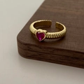 Dettaglio macro dell'anello dorato con zircone a cuore e texture a coste verticali - Anello d'oro con zircone rosa rosso