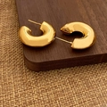 Dettaglio macro di orecchini a cerchio a C dorati lucidi su supporto in legno e lino - Orecchini a C da 2.5cm Oro