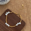 Dettaglio del bracciale con perle barocche, sfere dorate e ciondolo a cuore su legno - Bracciale / Oro
