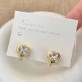Close-up of heart-shaped gold zircon hoop earrings on a white jewelry display card - Gold White Zircon Stud Earrings