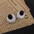 Primer plano de pendientes retro plateados con piedra ovalada negra sobre periódico viejo - Estilo de Ojo de Gato Negro Ovalado Plateado