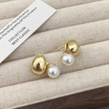 Dettaglio macro degli orecchini con perle e sfere dorate su vassoio in velluto beige - Oro