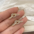 Nahaufnahme von goldenen Knotohrringen mit Zirkonia-Besatz, in der Hand gehalten - Knoten-Stil / Gold