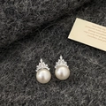 Detailed macro view of white pearl earrings with zircon crown setting on knit fabric - Crown Pearl Stud Earrings / Silver/White