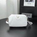 White quilted camera bag with green enamel butterfly and wide fabric strap on black desk - White