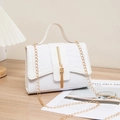 White faux crocodile skin crossbody bag with gold chain and fringe detail on wood - White