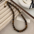 Gros plan d'un collier de perles oeil de tigre 8mm avec fermoir doré sur plateau bijoux - Diamètre de perle 8mm / Marron