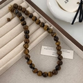 Détail d'un collier de perles en œil de tigre avec fermoir doré sur écrin à bijoux beige - Diamètre de perle 10mm / Marron