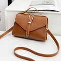 Brown minimalist crossbody bag with gold buckle and top handle on display stand - Brown