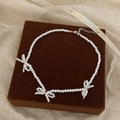 Detail of three pearl bow ties on a luxury necklace with golden clasp and velvet display - Bright Pearl Bow Beaded Necklace