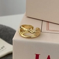 Detail of a minimalist gold-finished criss-cross ring on a soft pink gift box - Crisscross Style / Gold
